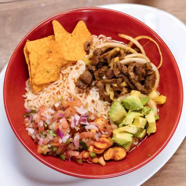 A red bowl of ramen with beef, avocado, pico de gallo, and tortilla chips.