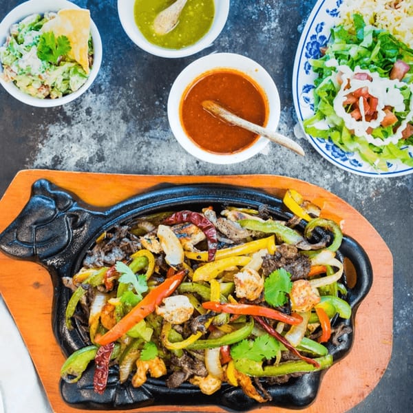 Sizzling fajitas with bell peppers and onions, served with guacamole, salsa, and a side salad.